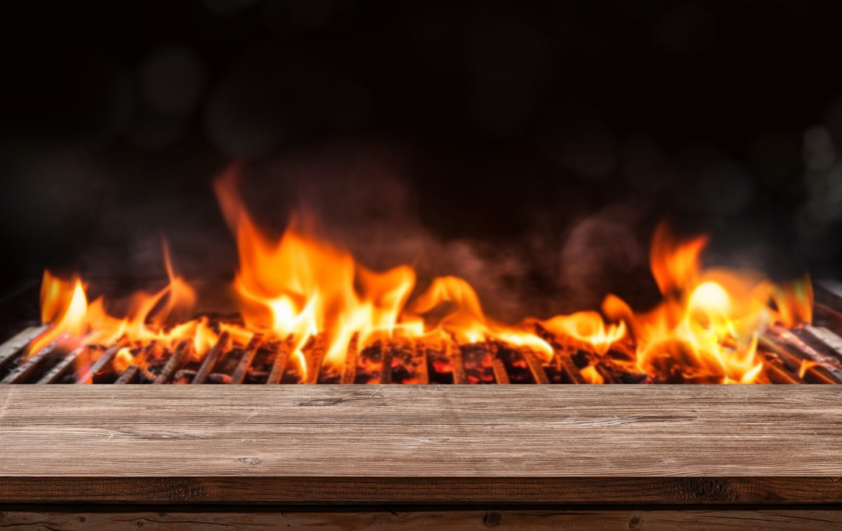 Barbecue BBQ grill with flaming fire and ember charcoal on black background, wooden table