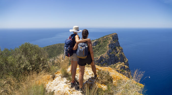 Two women hikers on mountain summit overlooking the mediterranean sea