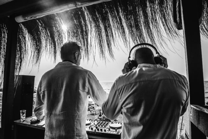 Back view of disc jockeys playing music for tourist people at club party outdoors on the beach - Djs wearing headphones at music live event - Music and fun concept - Black and white editing