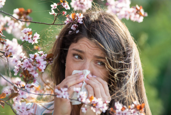 Girl wiping nose in front of blooming tree in spring