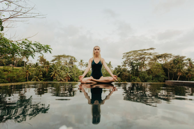 Blond woman in One Peice Swimsuit doing yoga at the edge of an infinity pool