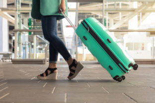 Close up detail of young woman walking with suitcase at the station. Turquoise jacket and suitcase. Business woman