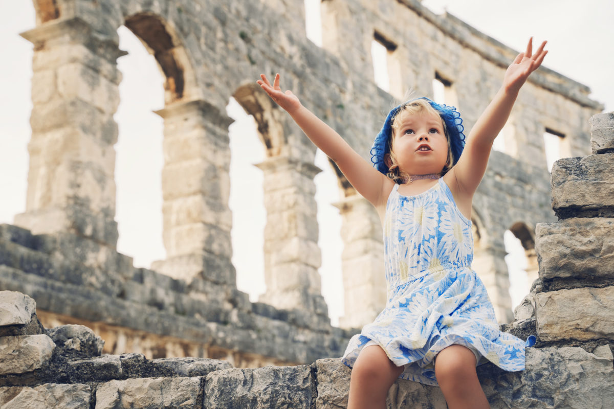Ute little girl with family exploring Roman Amphitheater Arena like as Coliseum - famous tourist travel destination in Pula, Croatia. A child plays in historical ruins of an ancient structure