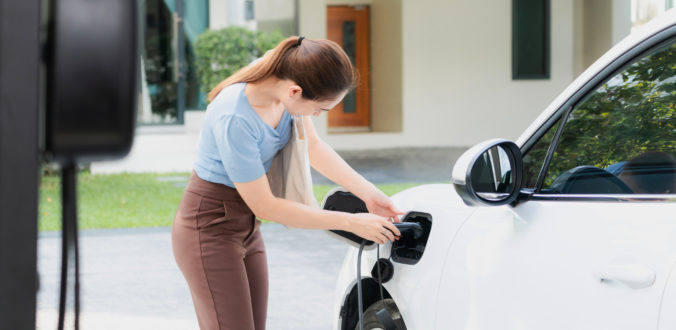 Progressive woman recharge her EV car at home charging station.