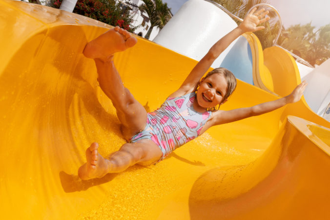 Happy child having fun on slide at outdoor water park. summer vacation