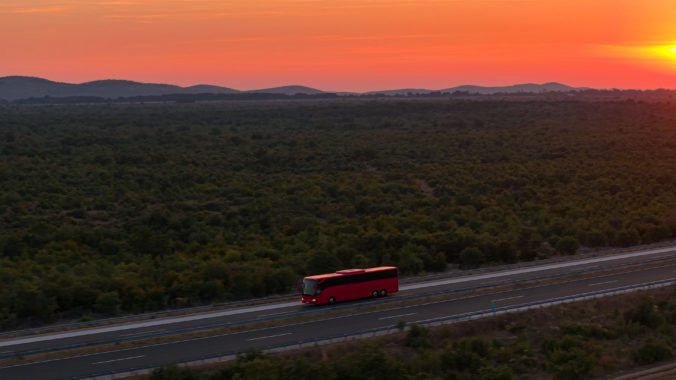 AERIAL: A red bus travels down the highway under a captivating crimson sunset.