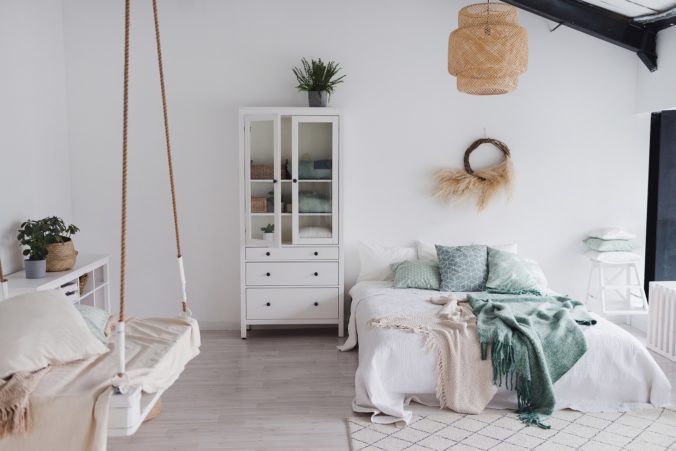 Modern scandinavian sunny bedroom with plants , white bedding and pillows. Space with white walls and wide window. Eco decor. Real photo.