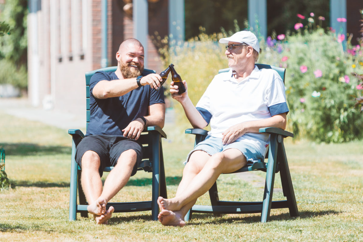 Two smiling men (young and old) drinking beer in the summer garden - best friends (father and son) toasting and laughing together - family and Father's Day celebration concept