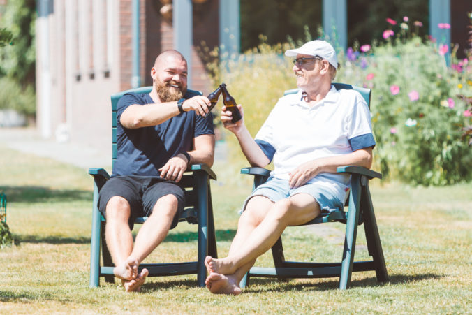 Two smiling men (young and old) drinking beer in the summer garden - best friends (father and son) toasting and laughing together - family and Father&#039;s Day celebration concept