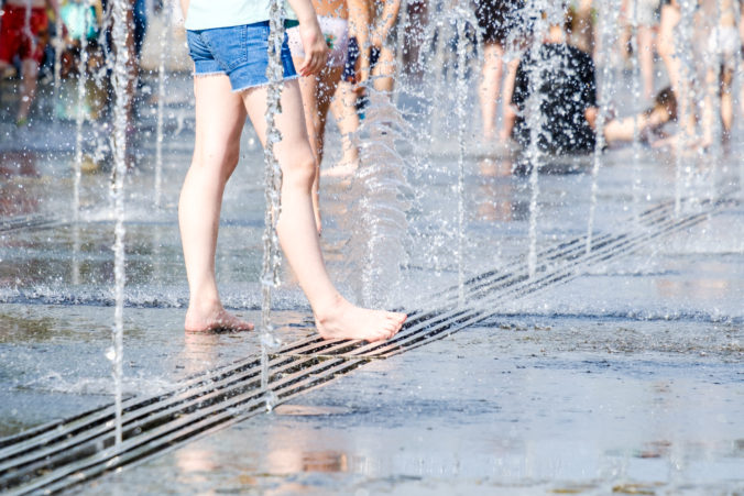 Selective focus on the bare feet of a woman in the splashes of jets of water from the fountain.