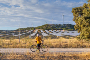 Man from behind leaning on bicycle looking at wind power towers and solar farm in rural setting at sunset