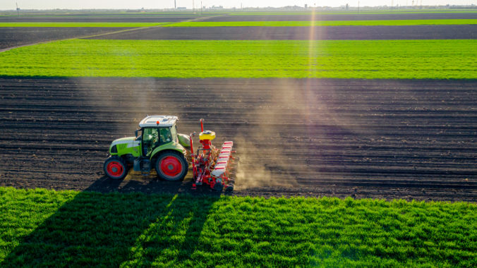 Aerial view of tractor as dragging a sowing machine over agricultural field, farmland