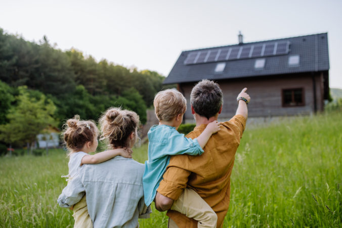 Happy family in front of their house with solar panels on the roof.