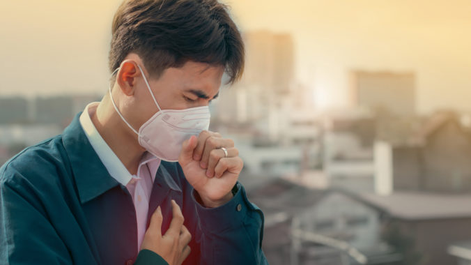 A young man wearing face masks to protect PM 2.5 smoke, city dust danger and air pollution in city, factory pipes and industrial smog. toxic mist. Protection against smoke. covid 19 protection. Fog.