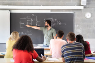 Young male teacher giving a science class explaining at the blackboard in a high school. Back to school. High school, education