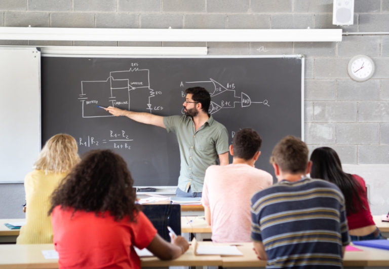 Young male teacher giving a science class explaining at the blackboard in a high school. Back to school. High school, education