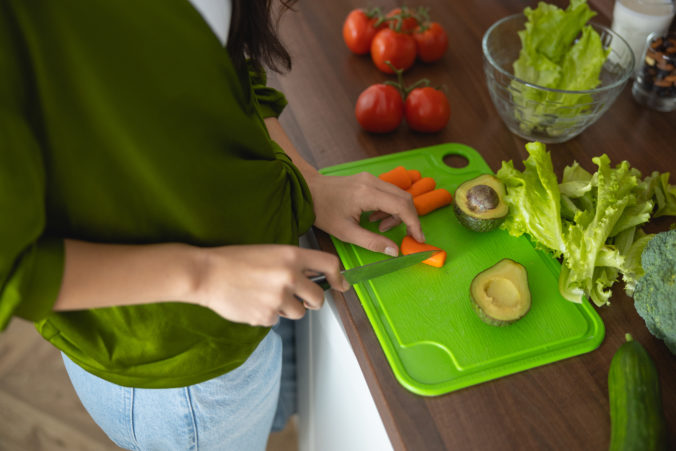 Hands cutting fresh vegetables on a plastic board