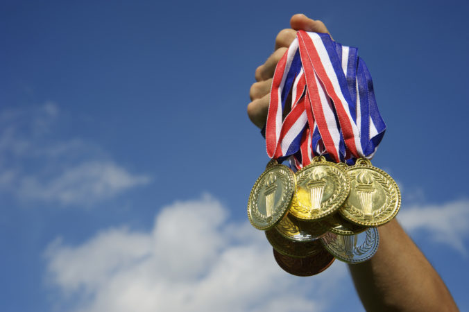 Athlete Hand Holding Up Bunch of Gold Medals Blue Sky