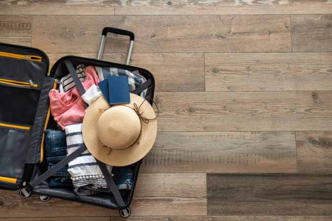 Open Suitcase with summer cloth, hat and passports on wooden background.