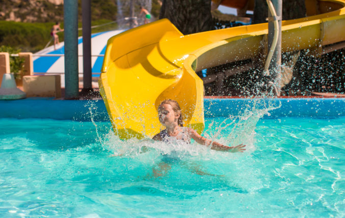 Little girl on water slide at aquapark during summer holiday