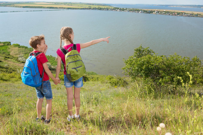 Teen boy and girl with backpacks on the back go on a hike, travel, beautiful landscape