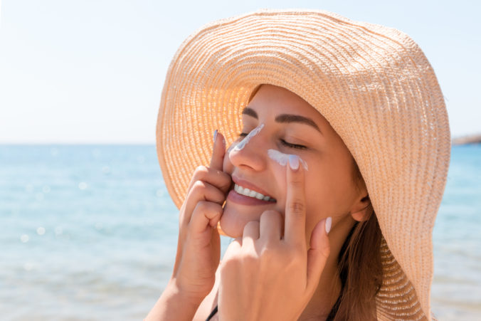 Smiling woman in hat is applying sunscreen on her face. Indian style