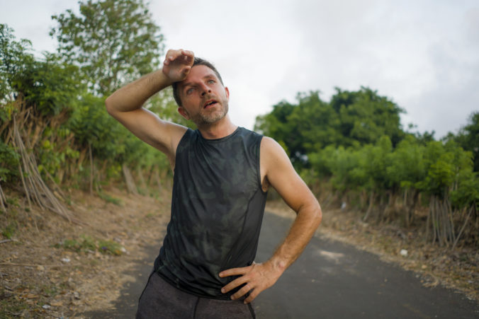 Sport and fitness lifestyle portrait of young attractive sweaty and tired man exhausted after outdoors running workout on beautiful country road breathing cooling off after training hard