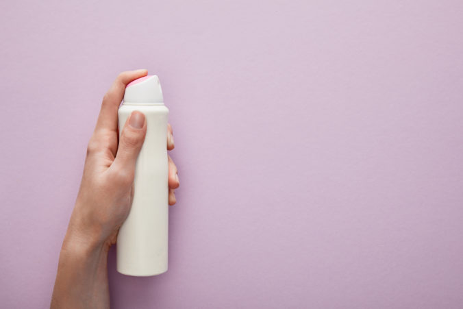 Cropped view of woman holding spray deodorant on violet background with white roses