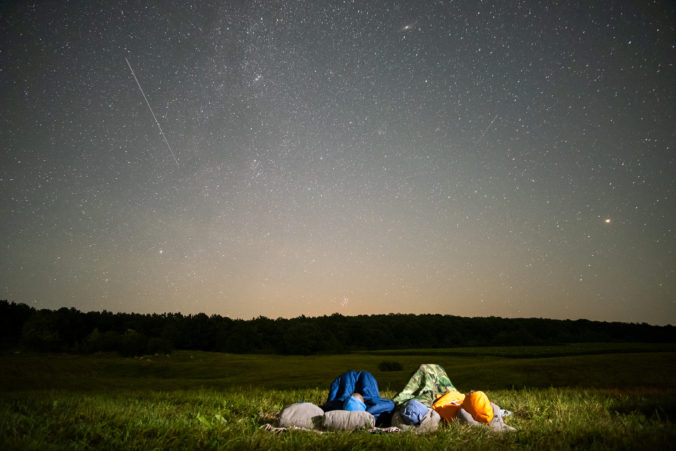 People resting in night field observing dark sky with many bright stars.