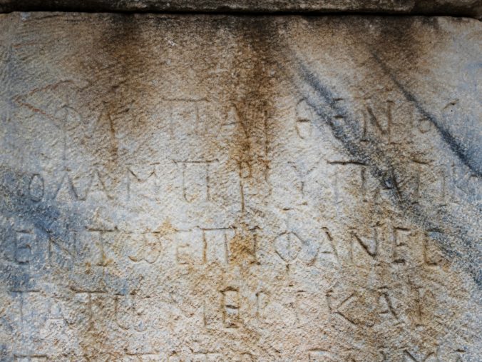 Ancient Greek inscription on a weathered stone surface with partially eroded and faded characters.