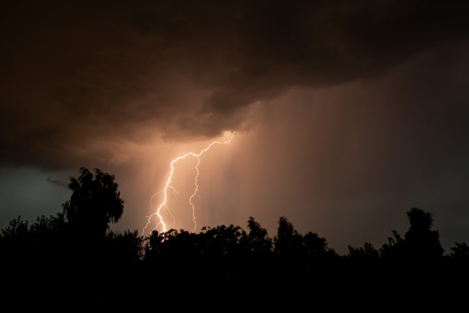 Beautiful lightning during a thunderstorm at night in a forest that caused a fire, against a dark sky with rain