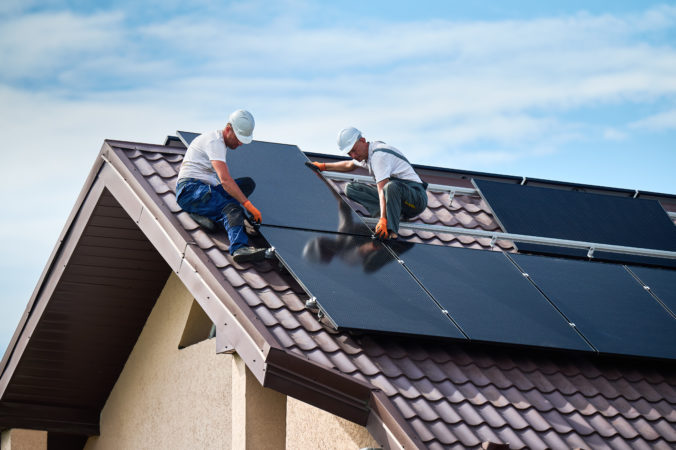 Workers building solar panel system on roof of house. Men installing photovoltaic solar module