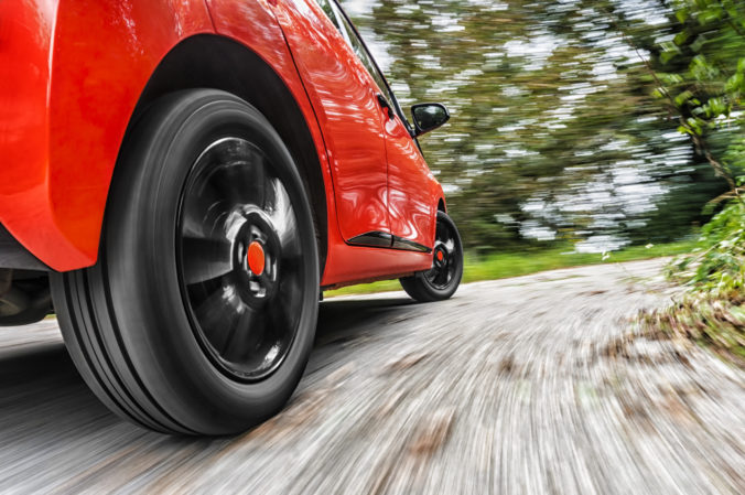 Focus on rear wheel of red car driving - blurry background