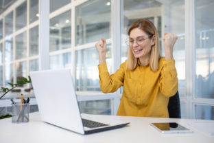 Excited businesswoman celebrating success at her office desk with laptop