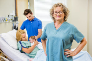 Mature Nurse Standing With Couple And Newborn Baby In Background