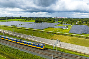 Railroad tracks with a train passing next to a field of solar panels seen from above