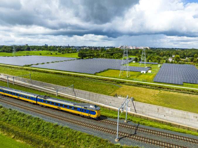 Railroad tracks with a train passing next to a field of solar panels seen from above