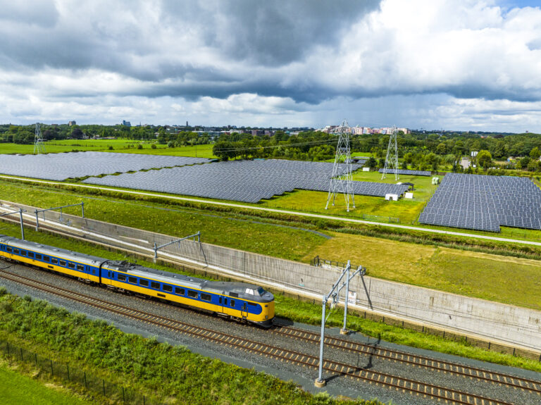 Railroad tracks with a train passing next to a field of solar panels seen from above