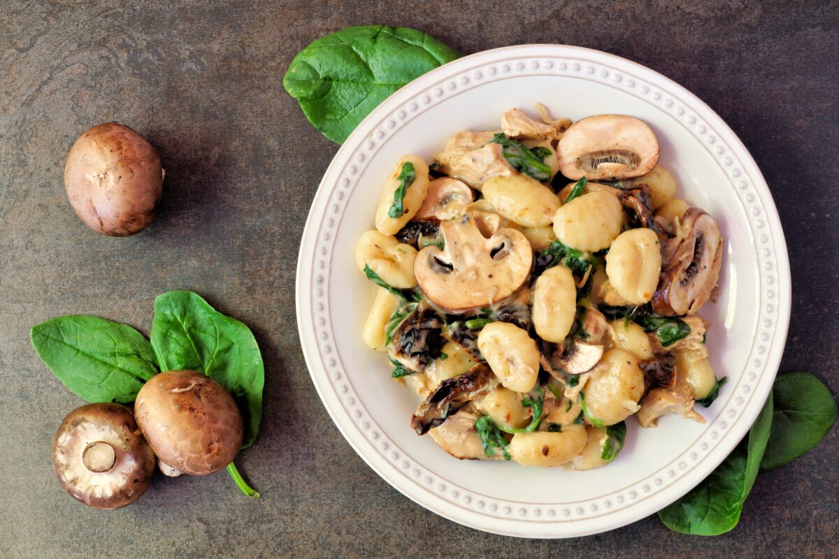 Gnocchi with mushroom sauce, spinach & chicken, top view on dark stone