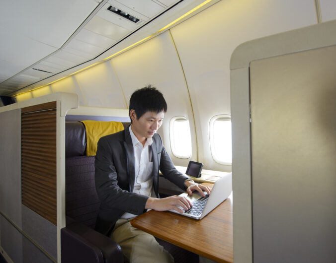 Asian man working with laptop on first class airplane