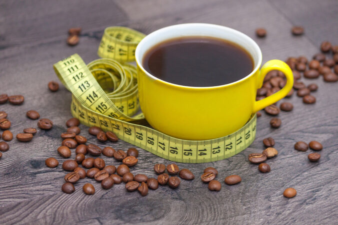 Yellow cup of coffee with beans and tape measure on wooden background.