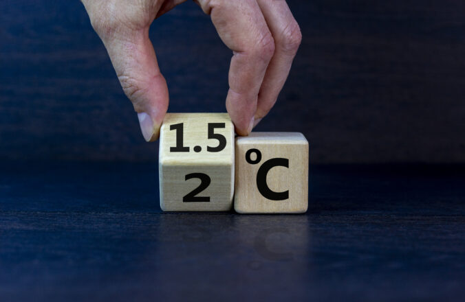 Symbol for limiting global warming. Male hand turnes a cube and changes the expression &#039;2 C&#039; to &#039;1.5 C&#039;, or vice versa. Concept. Beautiful dak wooden table, black background, copy space.