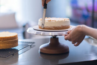 Skilled self made confectioner smearing white cream around cake layer made of lactose free products