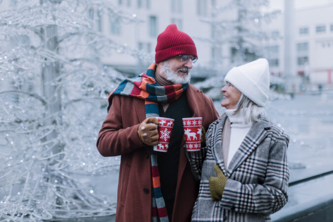 Happy senior couple enjoying christmas market, drinking muled wine.