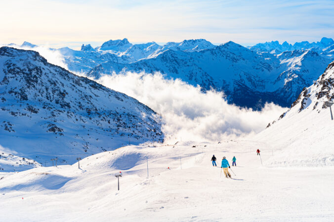 Dovolenkovanie na lyžiach. Lyžiari na zasnežených zjazdovkách v rakúskych Alpách s panoramatickým výhľadom na hory.