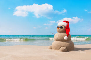 Christmas snowman in santa hat at sandy beach