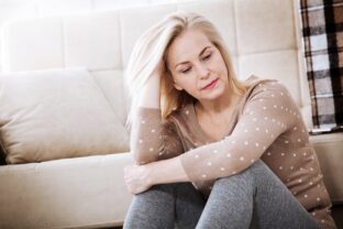 Hormonálna terapia v menopauze. Žena v strednom veku premýšľajúca, sediaca na pohovke, symbolizuje obdobie menopauzy a rozhodovanie o hormonálnej terapii.