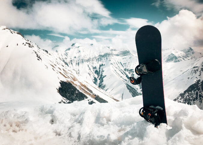 Snowboard stand in snow with beautiful white caucasus mountains background in Gudauri ski resort top viewpoint in winter. Georgia skiing winter holiday destination