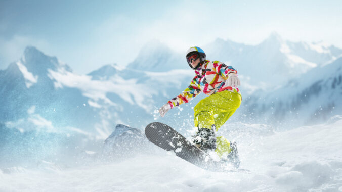 Young girl in sportswear sliding on snowboard over snowy mountains background. Winter activity