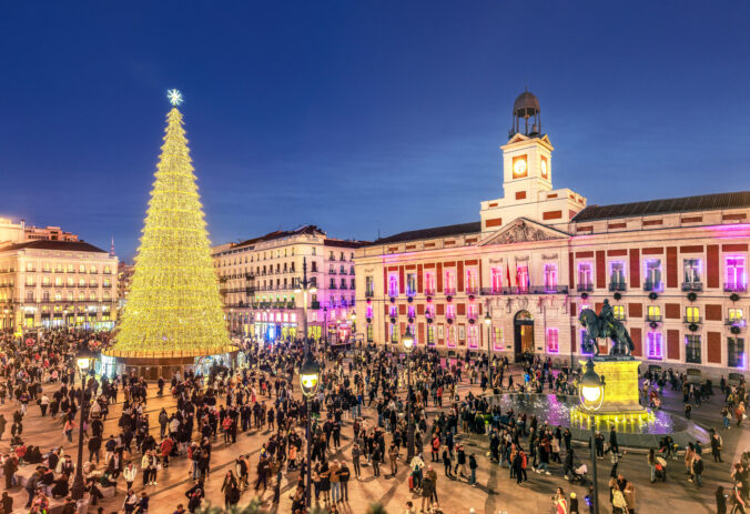 Festive crowd gathers around a great golden Christmas tree in the Puerta del Sol square, Madrid, Spain.